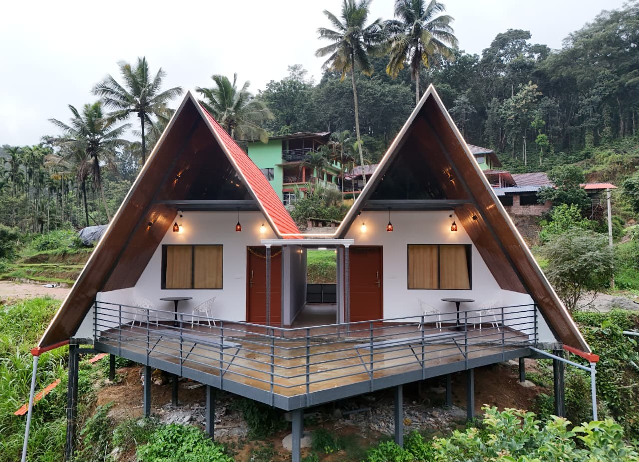Twin A-frame cottages on a raised deck at Coorg Natures Retreat, set against the Coorg hills and coffee plantation